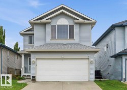 Two-story residence featuring light gray siding, a prominent arched window, a two-car garage, and an inviting front entrance with porch lighting - 