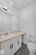 Bathroom featuring a white vanity with black hardware, an integrated sink, a large wall-mounted mirror, and wood-finish flooring - 