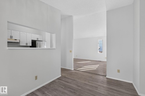 Open concept interior featuring wood-finish flooring, white walls, and a pass-through window to the kitchen with white cabinetry and a stainless steel refrigerator - 3722 34A Avenue Nw, Edmonton, AB - Indoor Photo Showing Other Room