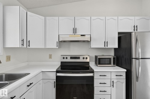 Kitchen featuring white cabinetry with black hardware, white countertops, stainless steel sink, black range, and stainless steel refrigerator - 3722 34A Avenue Nw, Edmonton, AB - Indoor Photo Showing Kitchen With Double Sink