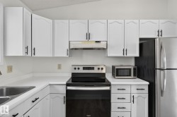 Kitchen featuring white cabinetry with black hardware, white countertops, stainless steel sink, black range, and stainless steel refrigerator - 