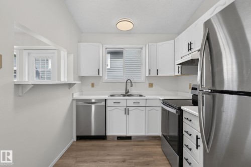 Kitchen featuring white cabinetry, stainless steel appliances, wood-finish flooring, a pass-through window, and a window above the sink - 3722 34A Avenue Nw, Edmonton, AB - Indoor Photo Showing Kitchen With Double Sink