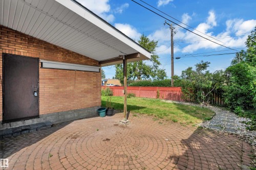 Brick exterior with a covered patio area featuring circular paver stones, a stone-lined pathway, and a green space - 8803 68A Street Nw, Edmonton, AB 