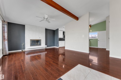 Vaulted ceilings with exposed wood beams, a white brick fireplace, wood-finish flooring, and a ceiling fan with integrated lighting - 8803 68A Street Nw, Edmonton, AB 