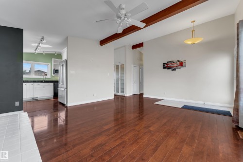 Vaulted ceilings with exposed beams, wood-finish flooring, white kitchen cabinetry with dark countertops, recessed kitchen lighting, and a ceiling fan - 8803 68A Street Nw, Edmonton, AB 