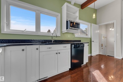 Bright, updated kitchen featuring white cabinetry with brushed metal hardware, black tile backsplash, stainless steel appliances including a black dishwasher and microwave, wood-finish flooring, and abundant natural light from dual windows - 8803 68A Street Nw, Edmonton, AB 