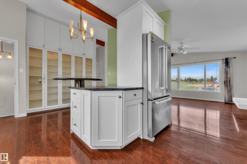 Hardwood-finish flooring, built-in cabinetry with glass-front doors, white kitchen cabinetry with dark countertops, stainless steel refrigerator, and large windows - 8803 68A Street Nw, Edmonton, AB 