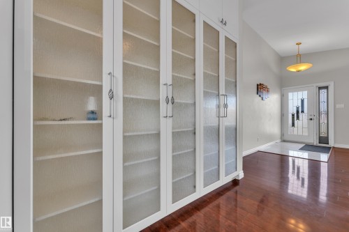 Built-in cabinetry with textured glass panels, rich wood-finish flooring, and a decorative pendant light fixture - 8803 68A Street Nw, Edmonton, AB 