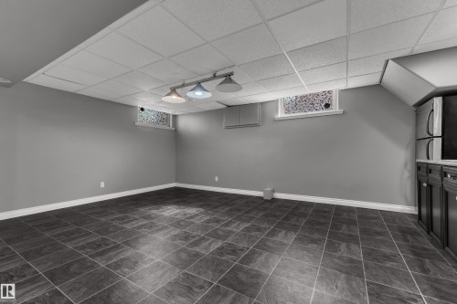 Spacious room featuring square tile flooring, a drop ceiling, and a built-in cabinetry unit with a refrigerator - 8803 68A Street Nw, Edmonton, AB 