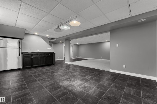 Spacious room featuring dark gray tile flooring, recessed lighting, and a built-in wet bar with dark wood cabinetry and a stainless steel sink - 8803 68A Street Nw, Edmonton, AB 