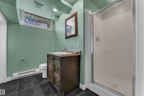 Bathroom featuring a dark wood-finish vanity with an integrated sink, a glass-enclosed shower, dark tiled flooring, a decorative transom window, and recessed lighting - 8803 68A Street Nw, Edmonton, AB 