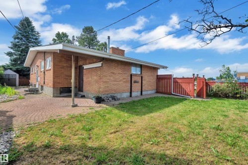 Brick exterior with a red-stained wood fence and gate, featuring a paved patio area and a separate storage shed - 8803 68A Street Nw, Edmonton, AB 