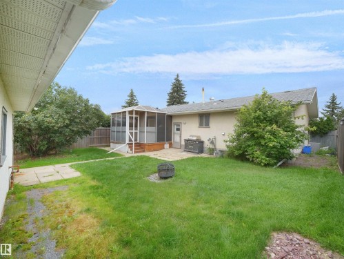 Expansive backyard featuring a screened-in porch with wood-finish decking, a concrete patio, and a privacy fence - 7435 32 Avenue Nw, Edmonton, AB 