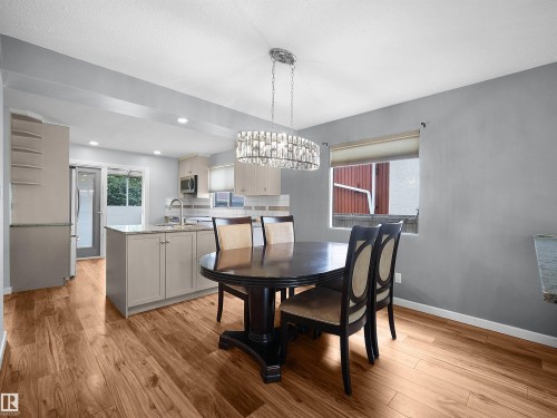 Recessed lighting, wood-finish flooring, kitchen island with built-in cabinetry, stainless steel appliances, and a crystal-style chandelier - 7435 32 Avenue Nw, Edmonton, AB 