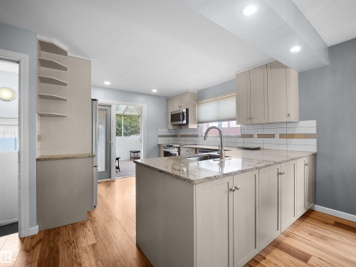 Kitchen featuring wood-finish flooring, granite countertops, white subway tile backsplash with accent strips, and light-toned cabinetry - 7435 32 Avenue Nw, Edmonton, AB 