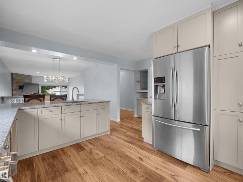 Modern kitchen featuring wood-finish flooring, light-toned cabinetry, stainless steel French door refrigerator, and a kitchen island with a basin sink and gooseneck faucet - 7435 32 Avenue Nw, Edmonton, AB 