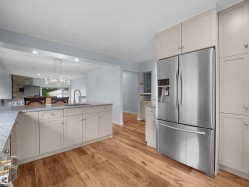 Modern kitchen featuring wood-finish flooring, light-toned cabinetry, stainless steel French door refrigerator, and a kitchen island with a basin sink and gooseneck faucet - 