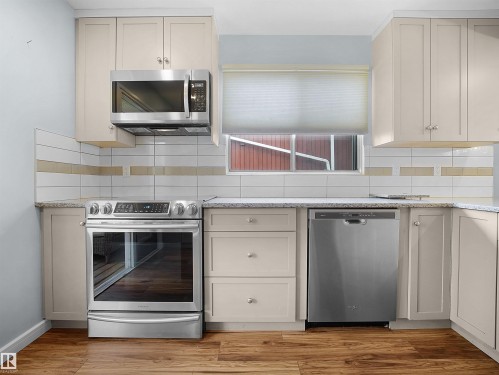 Wood-finish flooring, light-toned cabinetry, stainless steel appliances, speckled countertops, and a subway tile backsplash with accent band - 7435 32 Avenue Nw, Edmonton, AB 