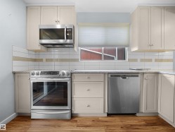 Wood-finish flooring, light-toned cabinetry, stainless steel appliances, speckled countertops, and a subway tile backsplash with accent band - 