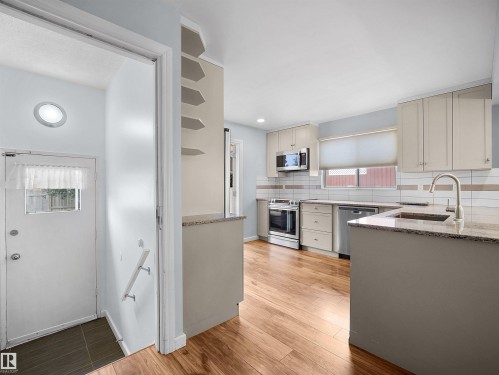 Kitchen featuring wood-finish flooring, stainless steel appliances, light cabinetry, a tile backsplash, and a sink with a gooseneck faucet - 7435 32 Avenue Nw, Edmonton, AB 