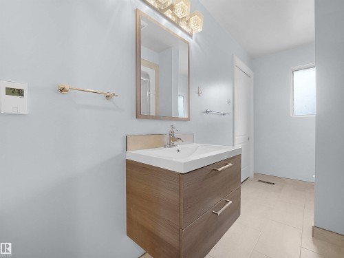 Floating wood-finish vanity with an integrated sink, polished chrome faucet, framed mirror, and decorative wall sconce - 7435 32 Avenue Nw, Edmonton, AB 