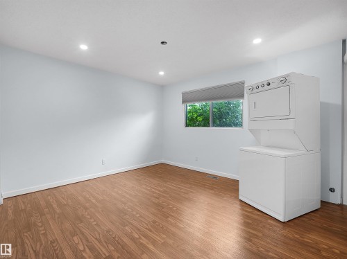 Wood-finish flooring, recessed lighting, window with roller shade, and a stacked washer and dryer unit - 7435 32 Avenue Nw, Edmonton, AB 