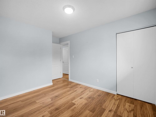 Wood-finish flooring, light blue wall paint, flush mount ceiling light, white bi-fold closet doors, and white interior door - 7435 32 Avenue Nw, Edmonton, AB 