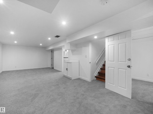 Expansive carpeted area featuring recessed lighting, a built-in cabinetry unit, and wood stairs with white risers - 7435 32 Avenue Nw, Edmonton, AB 