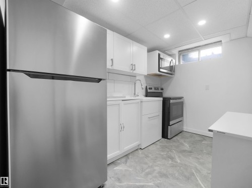 Kitchen with stainless steel appliances, white cabinetry, a built-in microwave, a stainless steel sink, and gray marble-look flooring - 7435 32 Avenue Nw, Edmonton, AB 