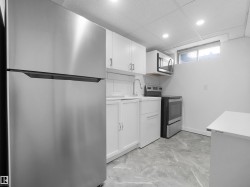 Kitchen with stainless steel appliances, white cabinetry, a built-in microwave, a stainless steel sink, and gray marble-look flooring - 