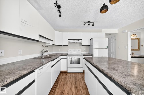 Galley kitchen featuring wood-finish flooring, white cabinetry with black hardware, and stone-look countertops - #30 300 Hooper Cr Nw, Edmonton, AB 