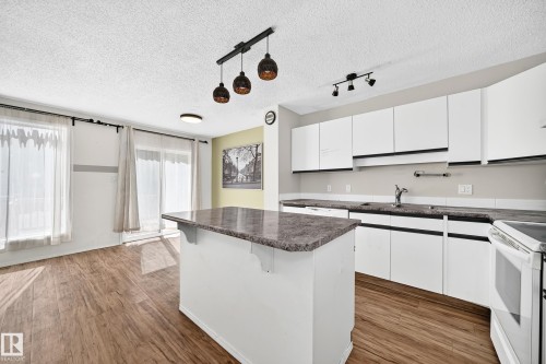 Open-concept living space with wood-finish flooring, white cabinetry, a kitchen island, and a sliding glass door - #30 300 Hooper Cr Nw, Edmonton, AB 