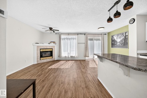 Wood-finish flooring, corner fireplace with tile surround, ceiling fan, and sliding glass doors - #30 300 Hooper Cr Nw, Edmonton, AB 