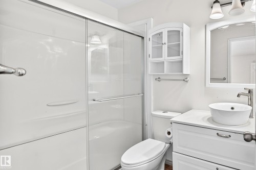 Shower with sliding glass enclosure, white vanity with integrated sink, wall-mounted mirror, and cabinet storage - #30 300 Hooper Cr Nw, Edmonton, AB 