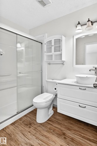Glass-enclosed shower, white vanity with integrated vessel sink, wall-mounted storage cabinet, wood-finish flooring, and vanity light fixture - #30 300 Hooper Cr Nw, Edmonton, AB 