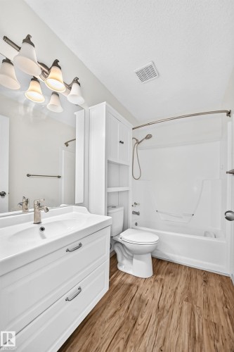 White vanity with dual drawers and integrated sink, brushed nickel faucet, wood-finish flooring, white tub with shower, and built-in storage cabinet - #30 300 Hooper Cr Nw, Edmonton, AB 