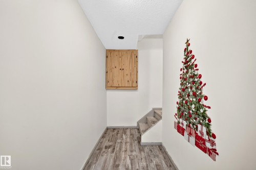 Wood-finish flooring leading to carpeted stairs, featuring a recessed ceiling light and built-in wood cabinetry - #30 300 Hooper Cr Nw, Edmonton, AB 