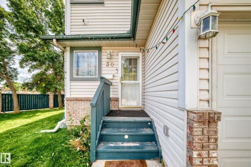 Entryway with brick detailing, light-colored siding, and a privacy fence - #30 300 Hooper Cr Nw, Edmonton, AB 