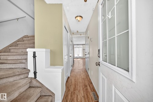 Entryway featuring wood-finish flooring, a white paneled front door with decorative glass, and a carpeted staircase with a handrail - #30 300 Hooper Cr Nw, Edmonton, AB 