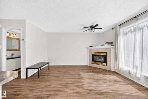 Wood-finish flooring, corner fireplace with tile surround, ceiling fan, and large window with curtain rod - #30 300 Hooper Cr Nw, Edmonton, AB 