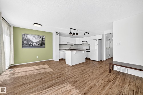 Open-concept layout with wood-finish flooring, a kitchen island, and white cabinetry - #30 300 Hooper Cr Nw, Edmonton, AB 