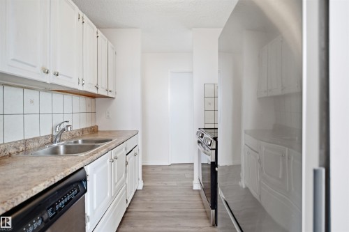 White cabinetry with chrome hardware, dual basin stainless steel sink, beige countertops, white tiled backsplash, and stainless steel dishwasher - #1115 13910 Stony Plain Rd Nw, Edmonton, AB 