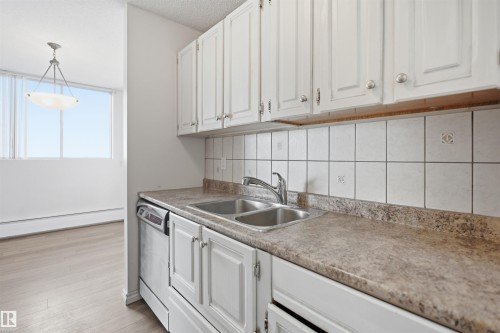 White cabinetry, stainless steel sink, tile backsplash, built-in dishwasher, and a light-colored countertop - #1115 13910 Stony Plain Rd Nw, Edmonton, AB 