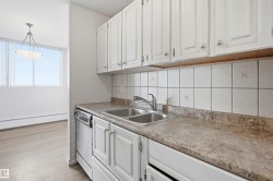 White cabinetry, stainless steel sink, tile backsplash, built-in dishwasher, and a light-colored countertop - 