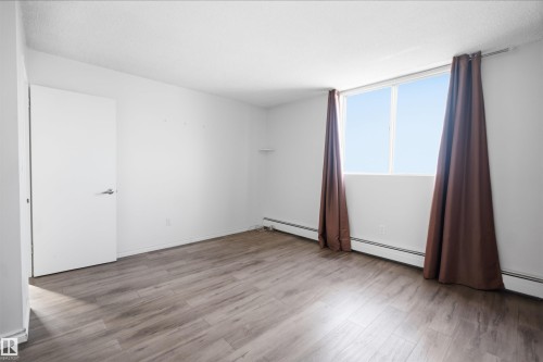 Bright interior with wood-finish flooring, a white door with a lever handle, and a large window - #1115 13910 Stony Plain Rd Nw, Edmonton, AB 