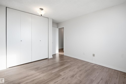 Wood-finish flooring with white baseboards, full-wall closet with bi-fold doors, white painted walls, and a ceiling-mounted light fixture - #1115 13910 Stony Plain Rd Nw, Edmonton, AB 