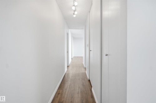 Hallway featuring wood-finish flooring, recessed lighting, and white panel doors - #1115 13910 Stony Plain Rd Nw, Edmonton, AB 