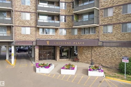 Brick facade building featuring multiple balconies, a covered entrance, and a ground-level parking area - #1115 13910 Stony Plain Rd Nw, Edmonton, AB 