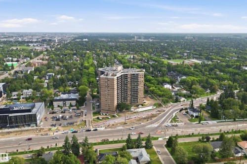 High-rise building featuring a brick facade and multiple balconies, surrounded by a broad urban landscape with extensive tree cover and a visible road network - #1115 13910 Stony Plain Rd Nw, Edmonton, AB 