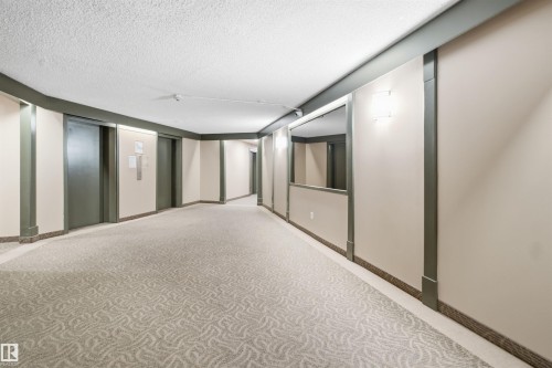 Carpeted hallway featuring wall sconces, accent trim, and a built-in mirror - #1115 13910 Stony Plain Rd Nw, Edmonton, AB 